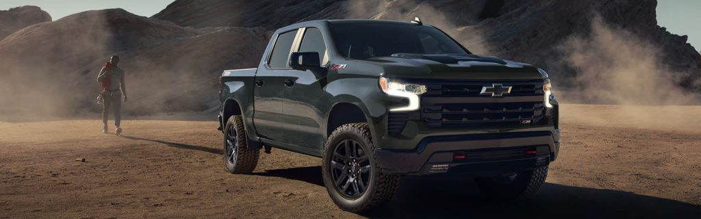 A dark green Chevrolet Silverado Z71 off-roading in a desert landscape with a person walking in the background.
