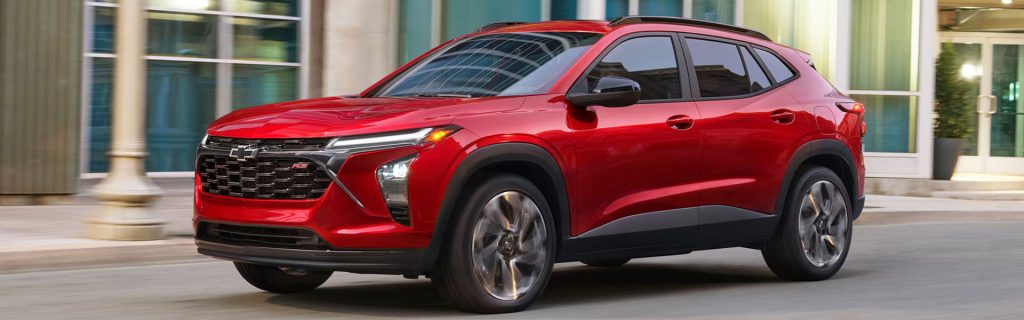 A red Chevrolet Trax RS driving through an urban street with modern buildings in the background.